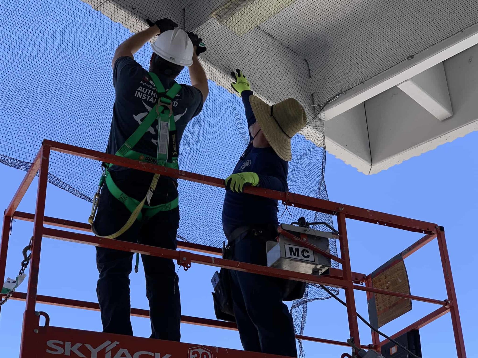 Two guys on a lift installing bird netting